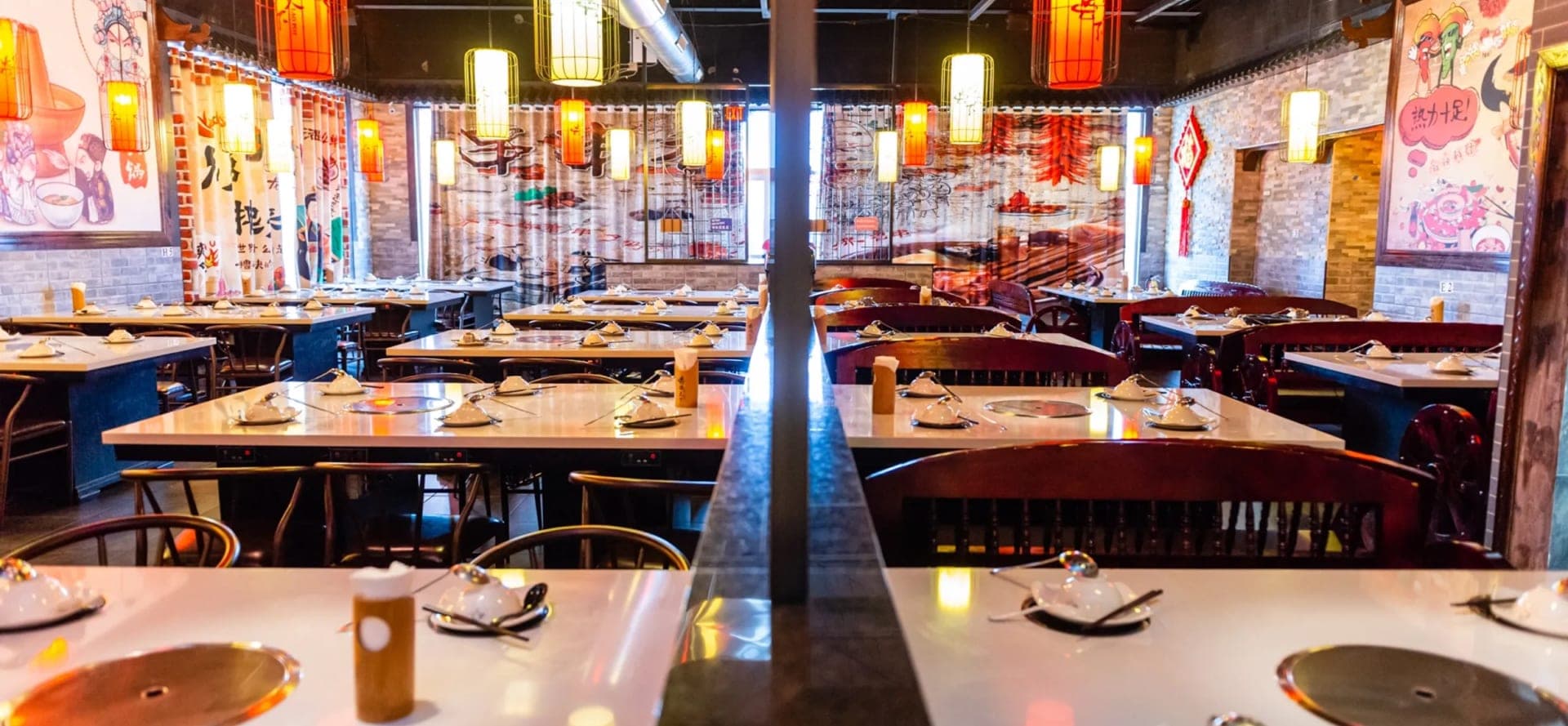 The Lao Pot dining room: rows of tables with built-in induction burners, red banquettes, brick walls and hanging lanterns.